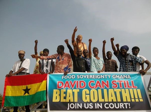 people with fists up holding a banner that says David can still beat Goliath; Join us in court!